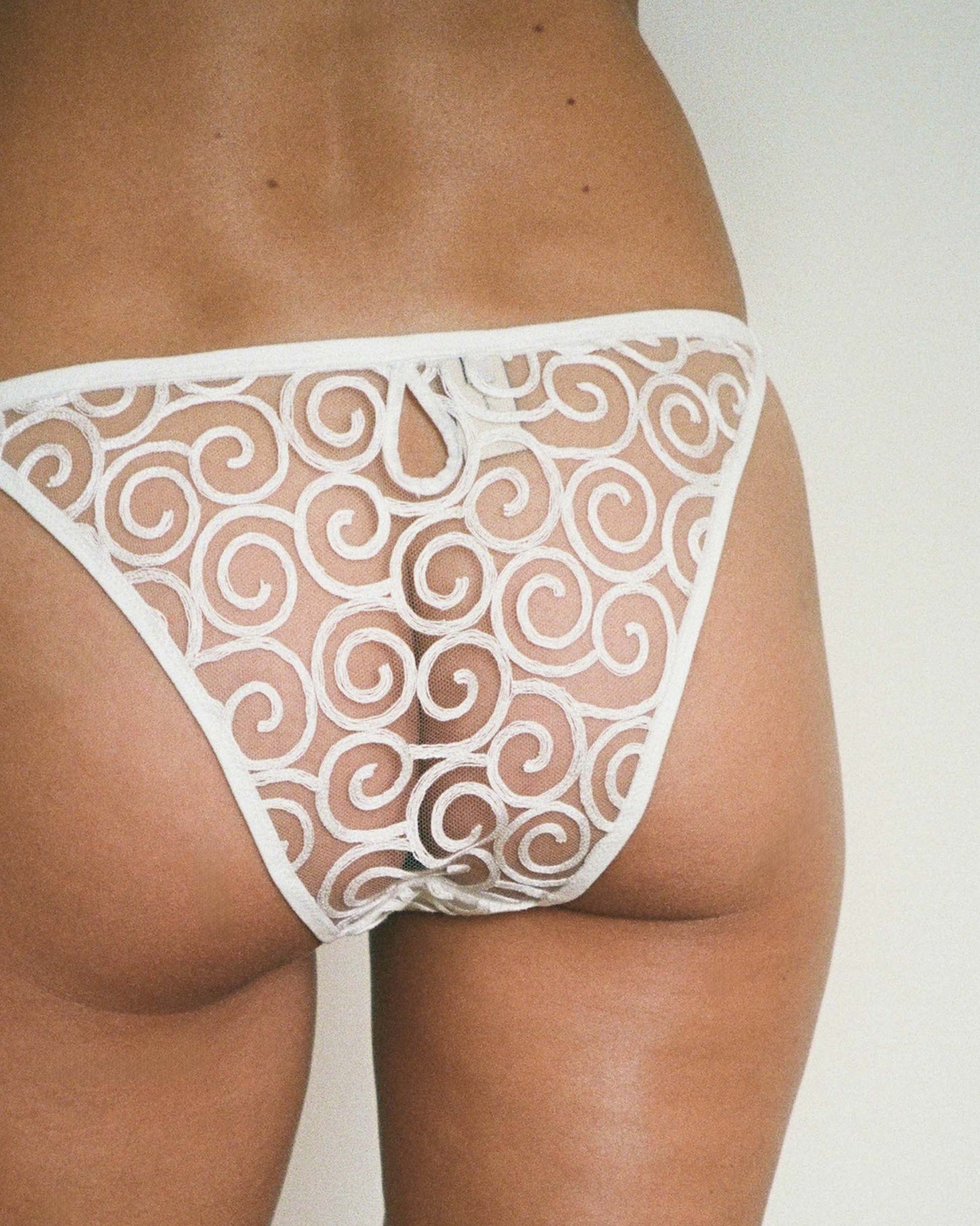 White lace thong worn by a person on a plain background