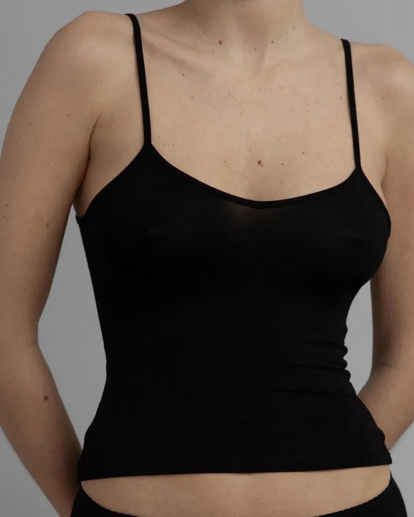 Black spaghetti strap top worn by a person on a gray background