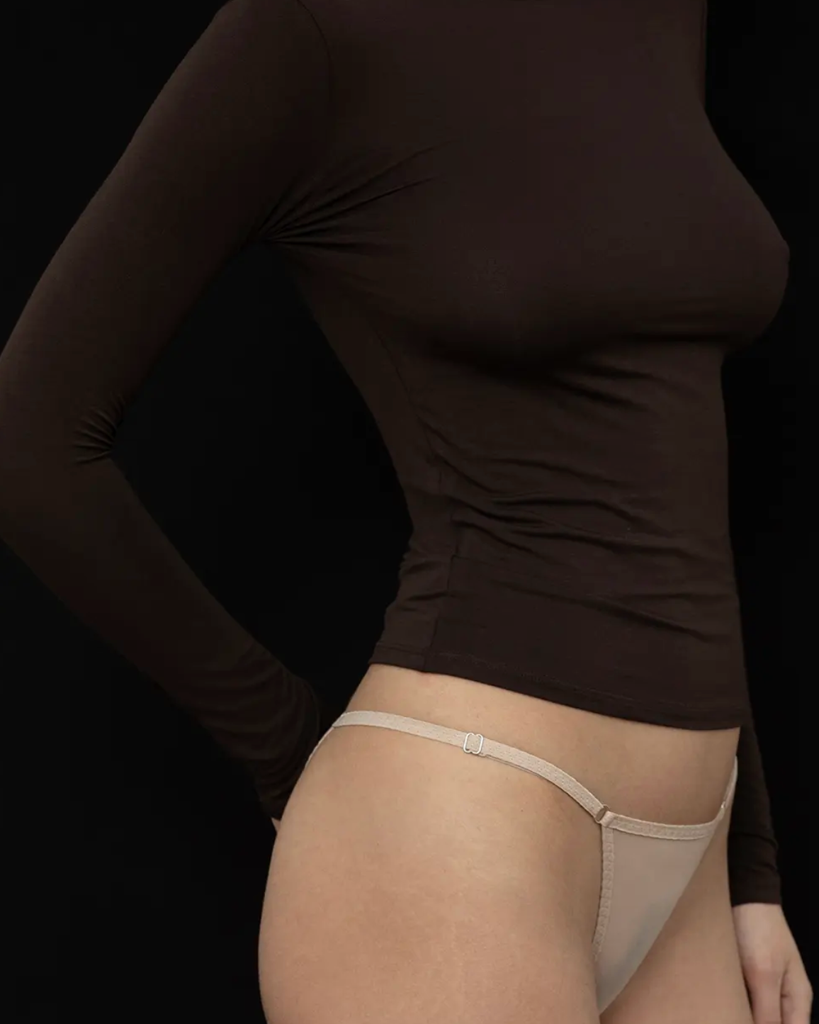 Person wearing a black long-sleeve top and beige underwear on a black background