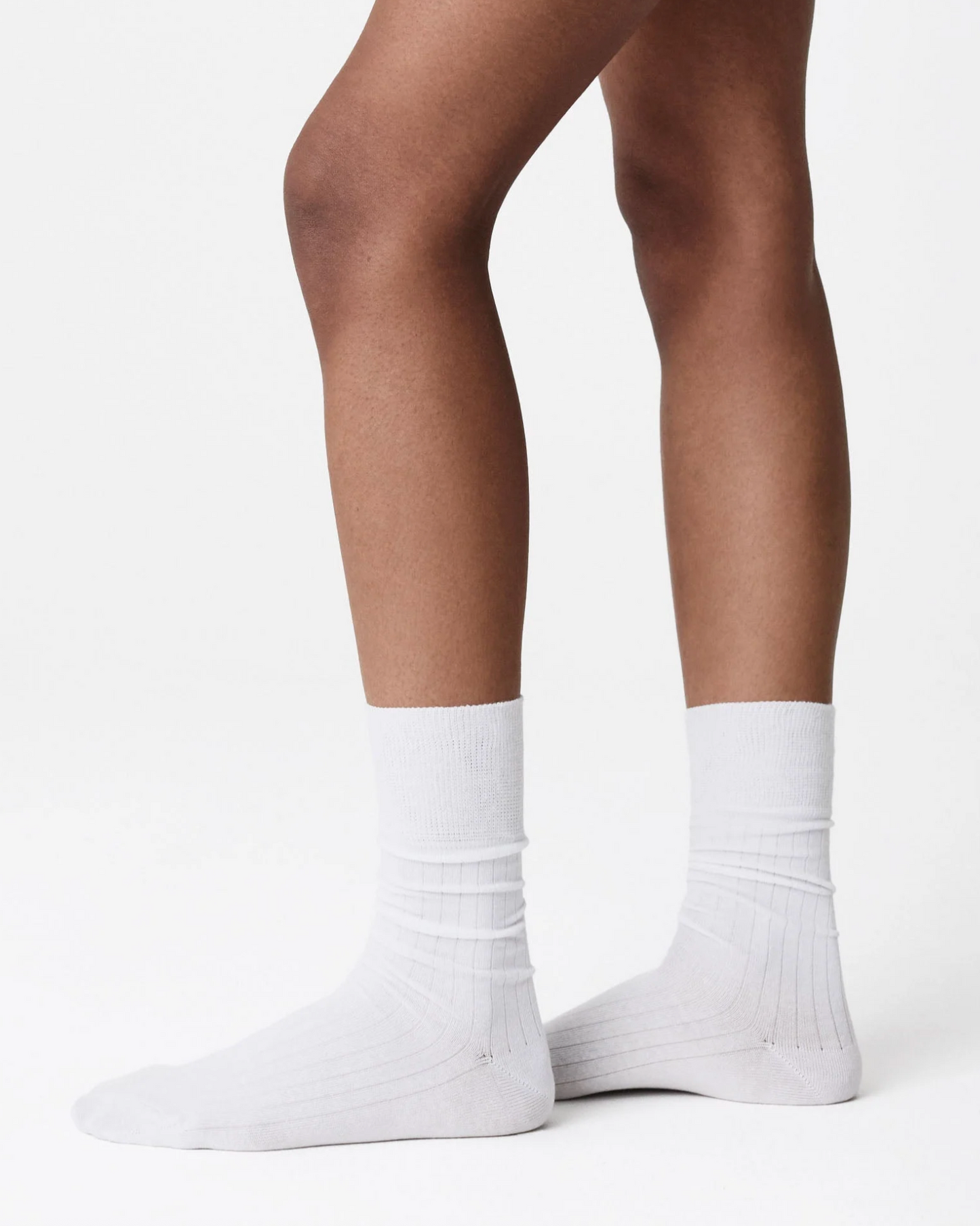 A close-up of a person's legs wearing plain white crew socks against a clean white studio background.