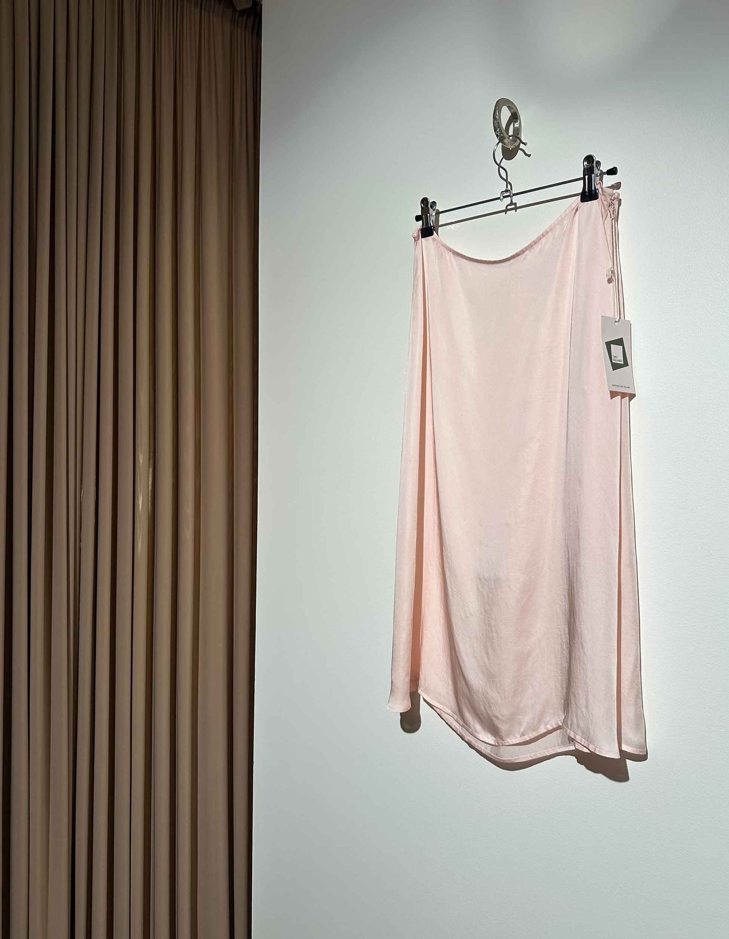 Pink slip skirt hanging on a rack against a neutral wall.