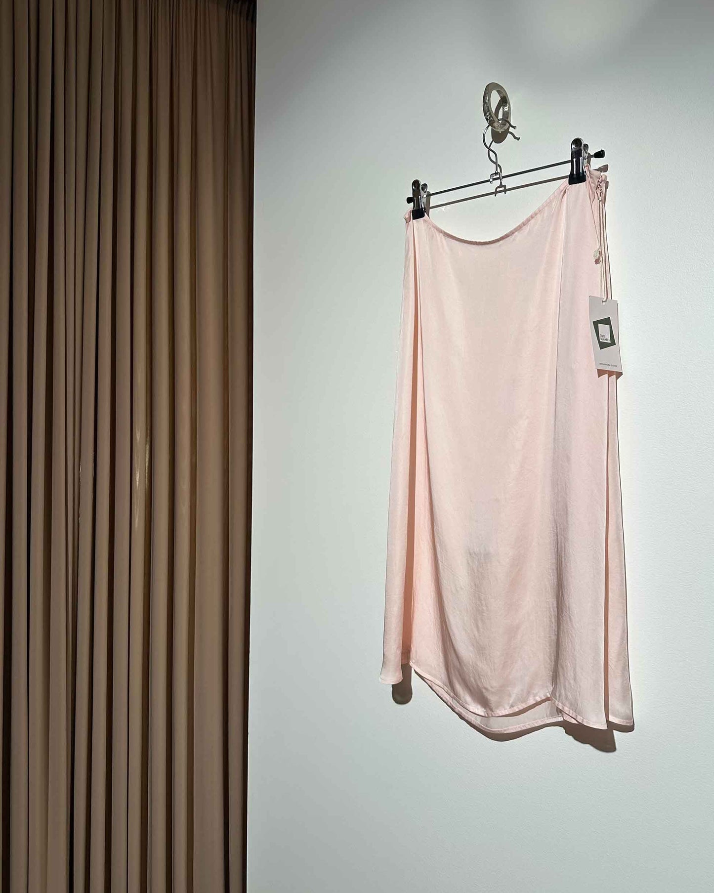 Pink slip skirt hanging on a rack against a neutral wall.