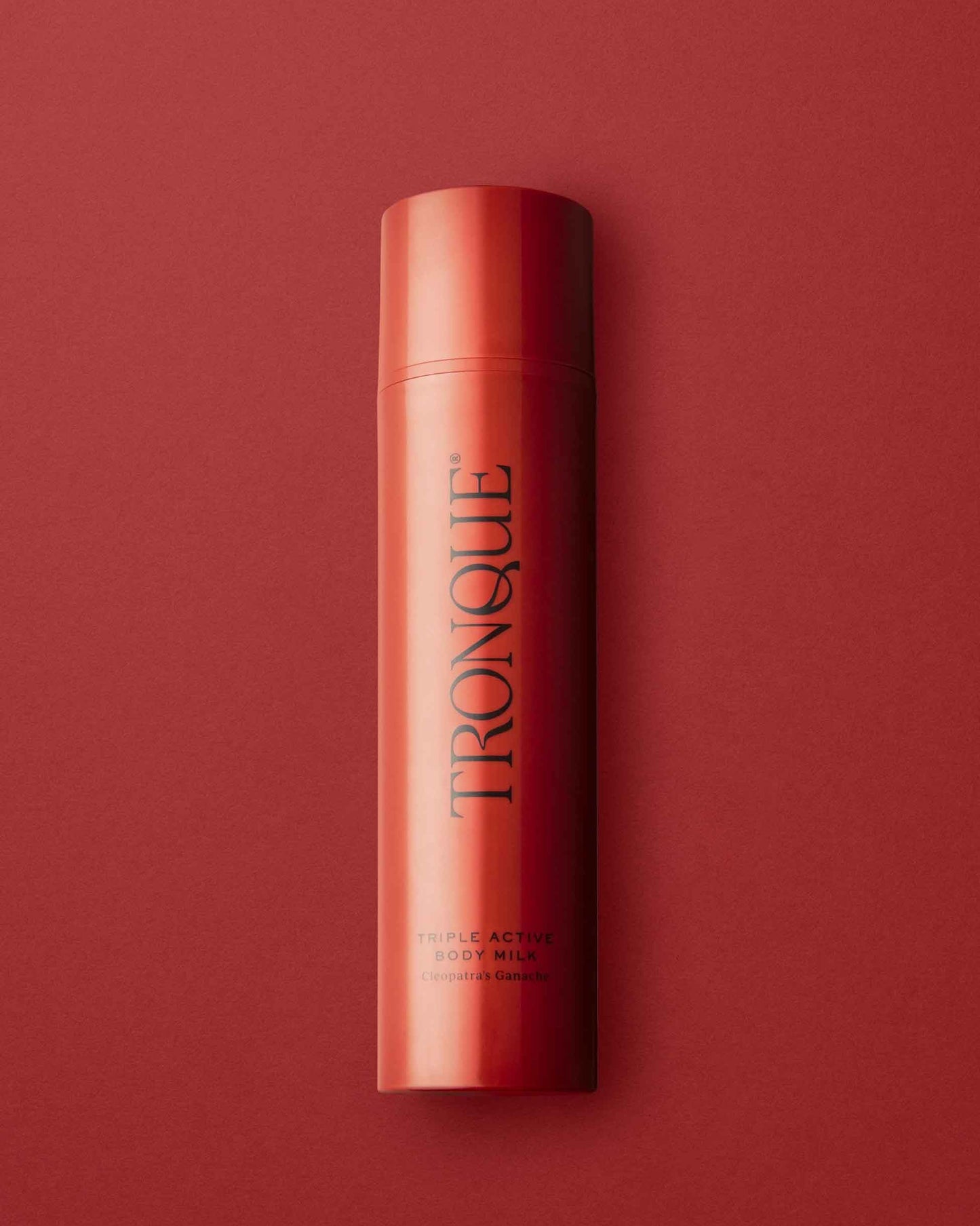 A single cylindrical bottle of Tronque Duplex Active Body Milk in a vibrant red-orange color, standing vertically against a matching red-orange background. The brand name 'TRONQUE' is printed vertically in black on the front of the bottle.