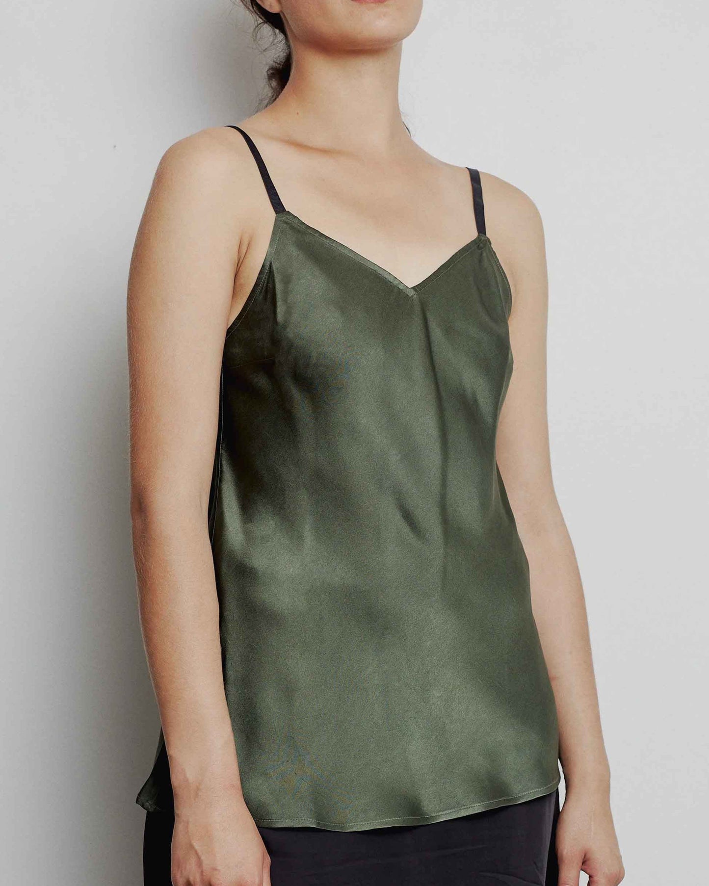A woman wearing a green silk camisole top with adjustable straps and a gentle v-neckline, paired with a black skirt.