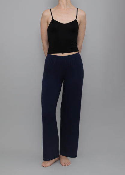 A model wearing a black spaghetti-strap crop top and navy blue wide-leg pants, standing against a solid gray studio background.