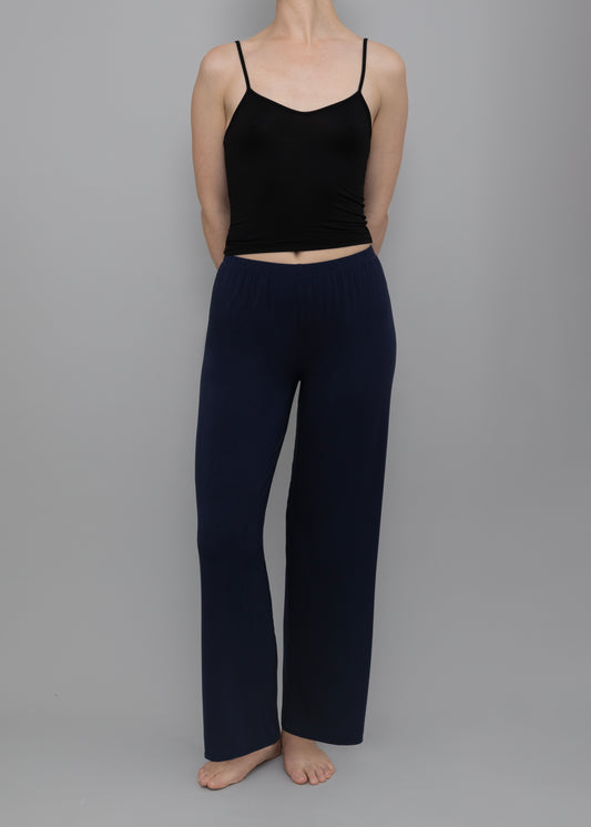 A model wearing a black spaghetti-strap crop top and navy blue wide-leg pants, standing against a solid gray studio background.