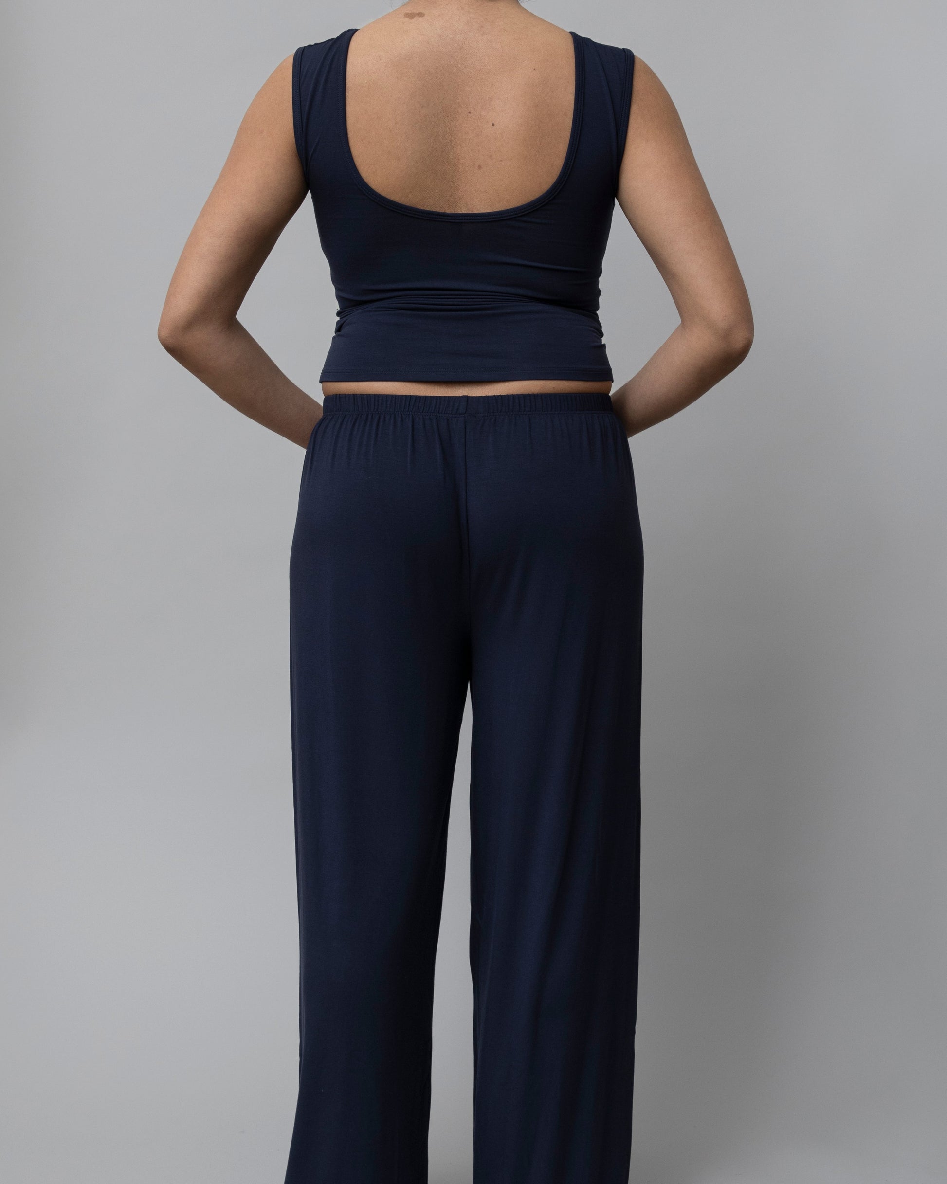 A model shown from the back wearing a dark navy blue sleeveless crop top and matching wide-leg pants against a solid gray studio background.