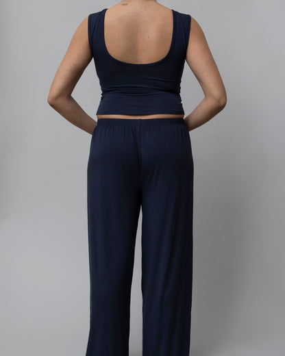 A model shown from the back wearing a dark navy blue sleeveless crop top and matching wide-leg pants against a solid gray studio background.