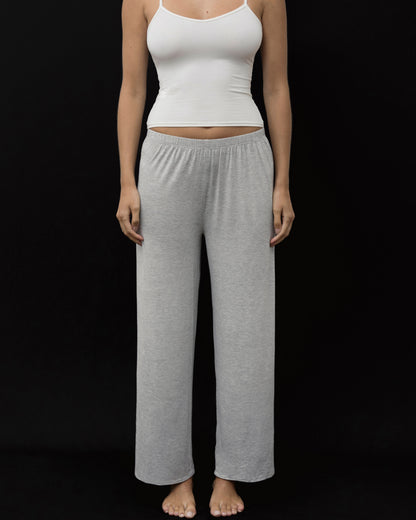 A woman modeling a two-piece loungewear set consisting of a white ribbed camisole top and heather gray wide-leg sweatpants, standing against a solid black background.