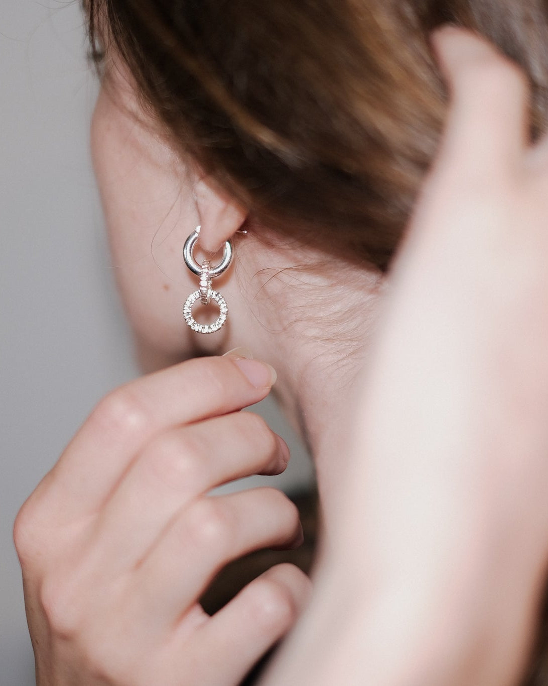 close up of ear with silver earring, with hand reaching to it from the rear.