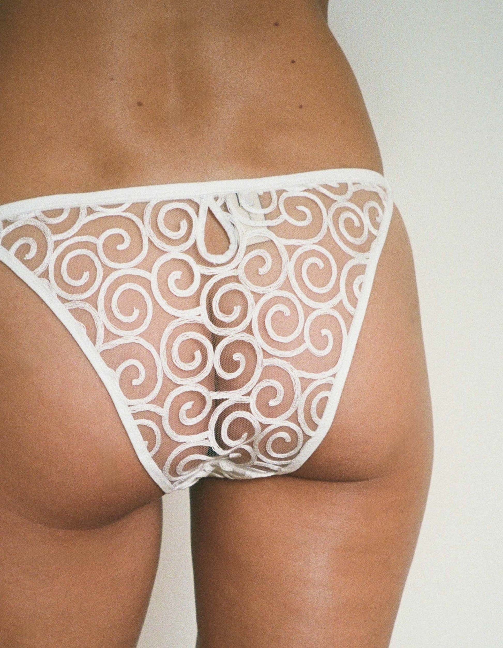White lace thong worn by a person on a plain background