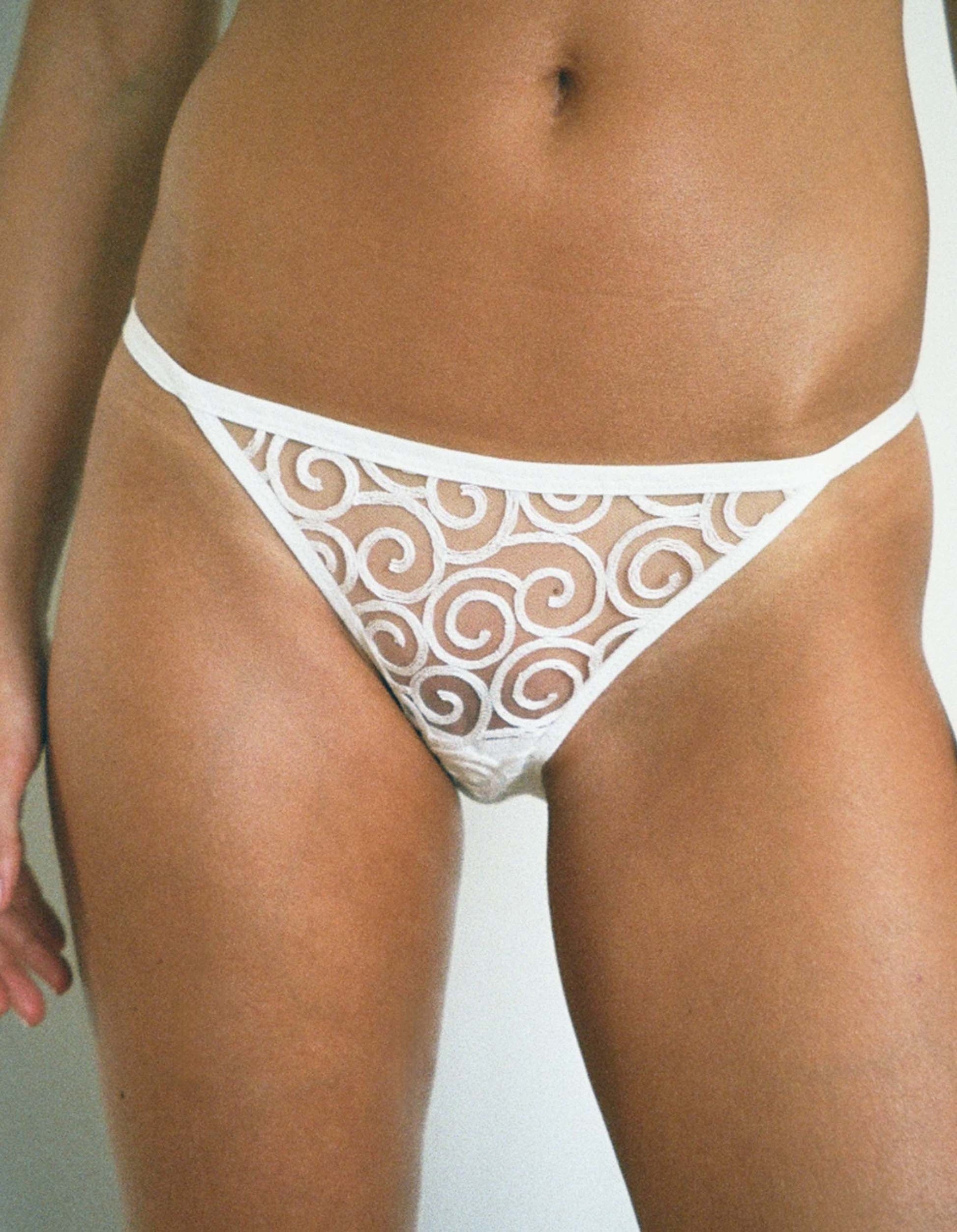 White lace thong worn by a person on a plain background