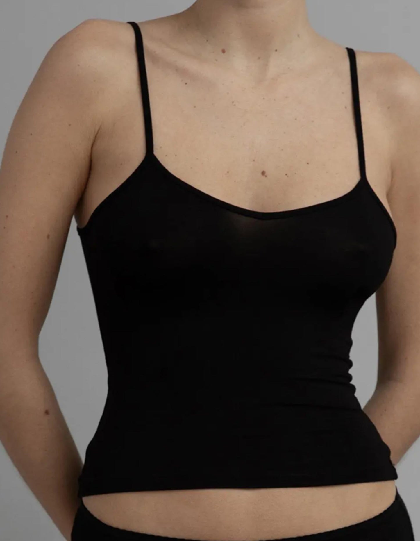 Black spaghetti strap top worn by a person on a gray background