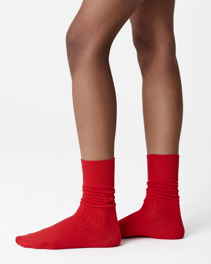 A close-up of a person's legs wearing bright red crew socks against a clean white studio background.