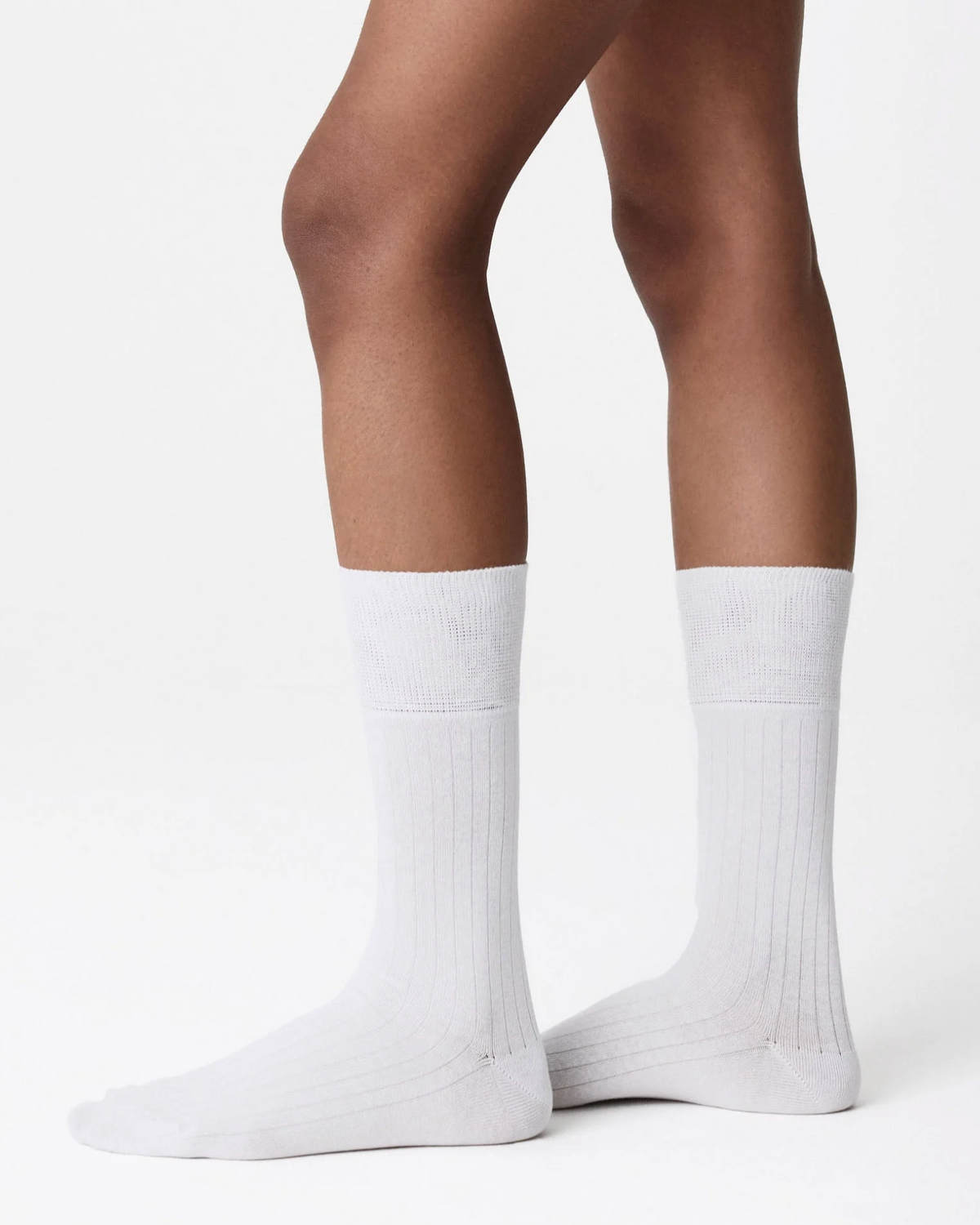 A pair of white ribbed crew socks worn on a model's feet, shown from the calf down against a clean white studio background.