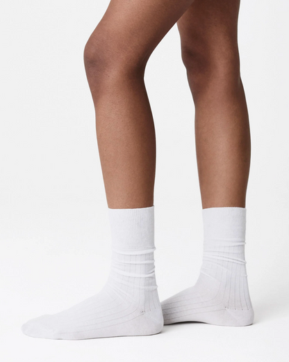 A close-up of a person's legs wearing plain white crew socks against a clean white studio background.