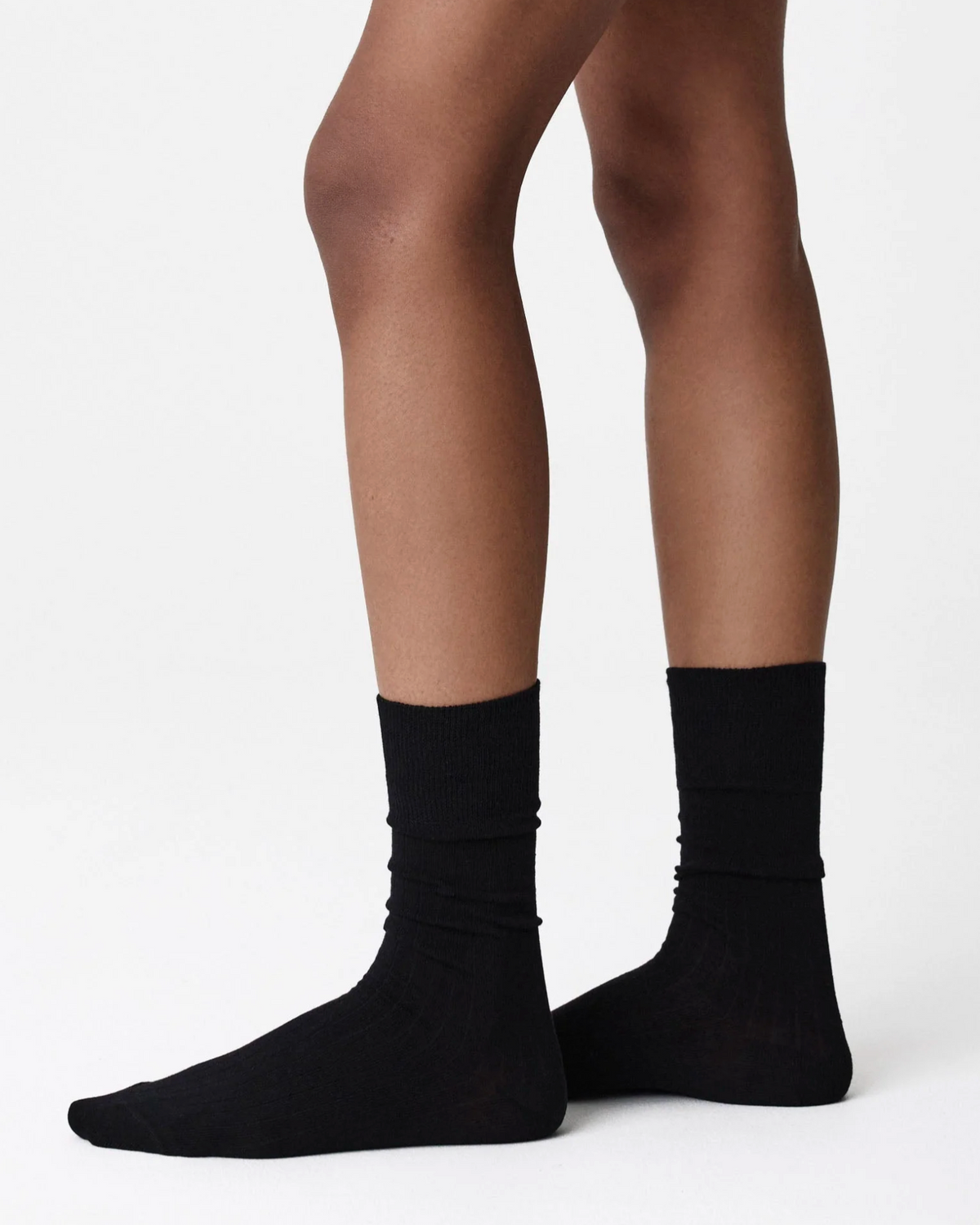 A close-up of a person's legs wearing a pair of black ribbed crew socks against a plain white studio background.