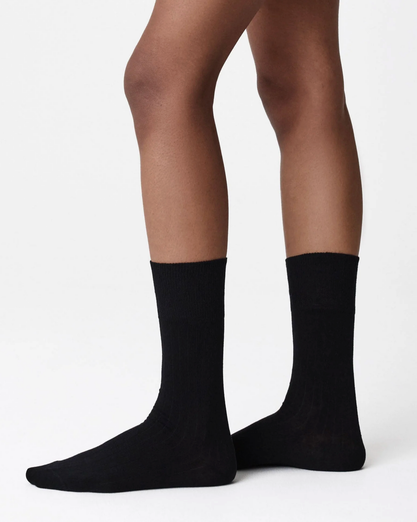 A pair of black crew socks worn on a person's feet, shown from the side against a clean white studio background.