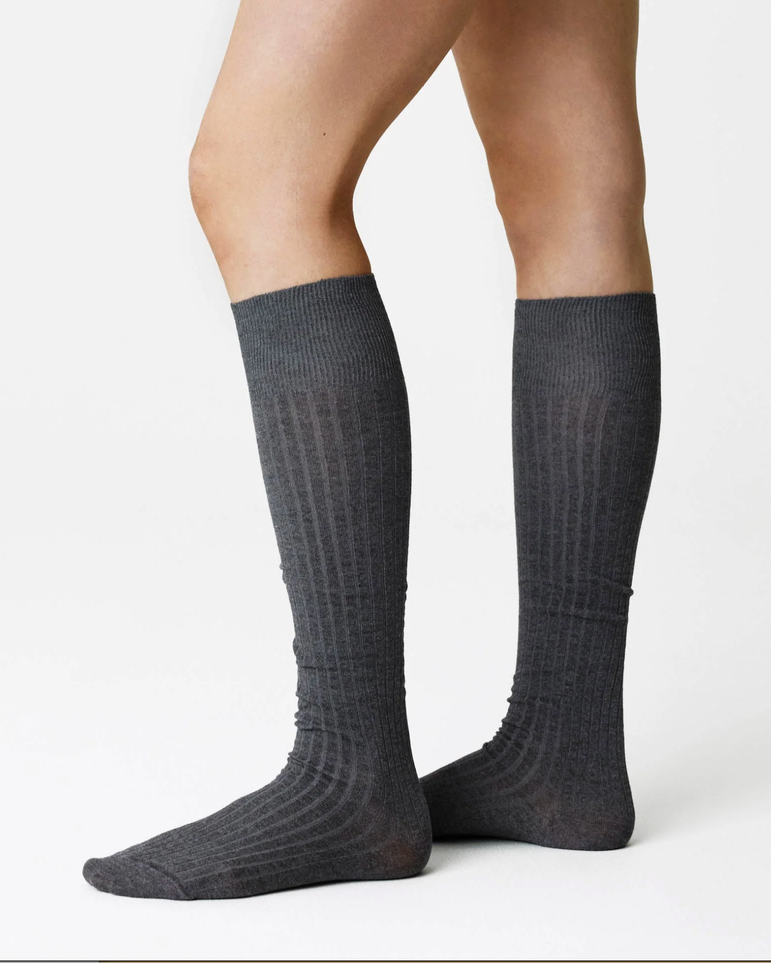 A pair of dark gray ribbed knee-high socks worn on a model's legs, shown against a plain white studio background.