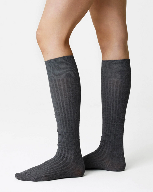 A pair of dark gray ribbed knee-high socks worn on a model's legs, shown against a plain white studio background.
