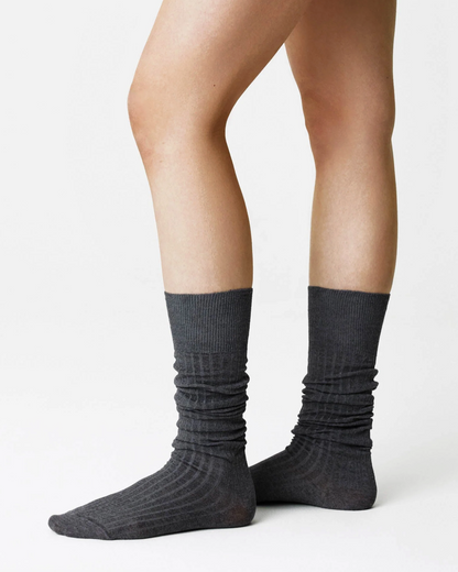 A person's legs wearing dark gray ribbed crew socks, shown from the feet up against a clean white studio background.