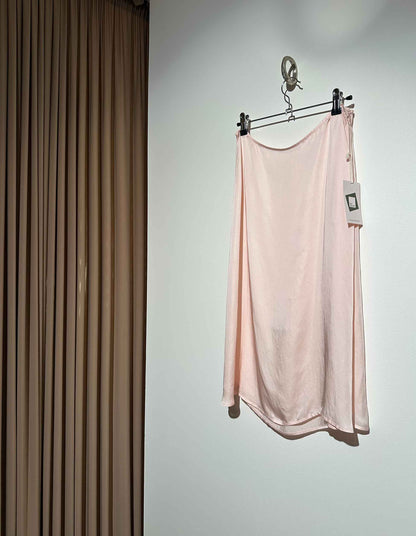 Pink slip skirt hanging on a rack against a neutral wall.