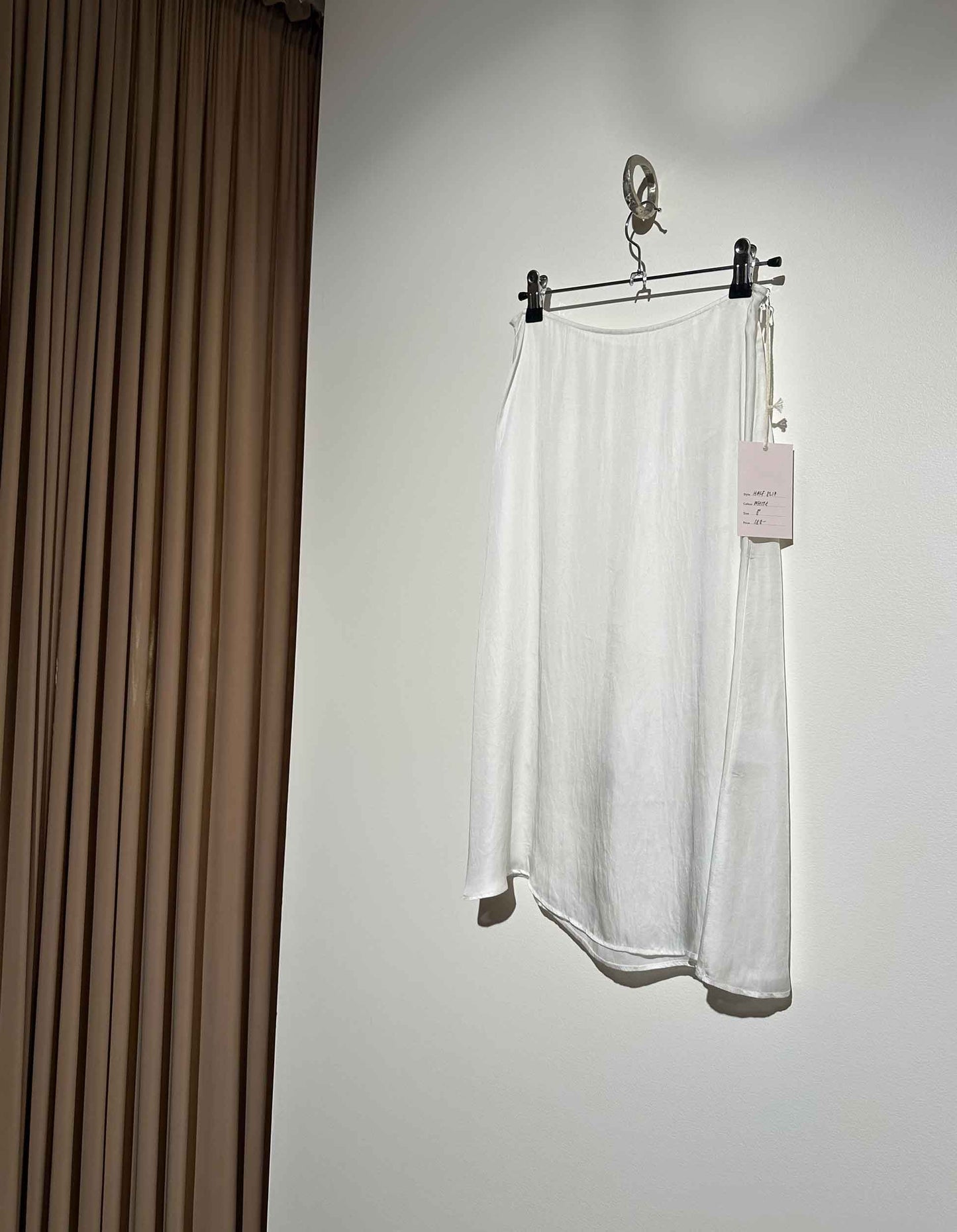 White skirt hanging on a rack against a plain wall.
