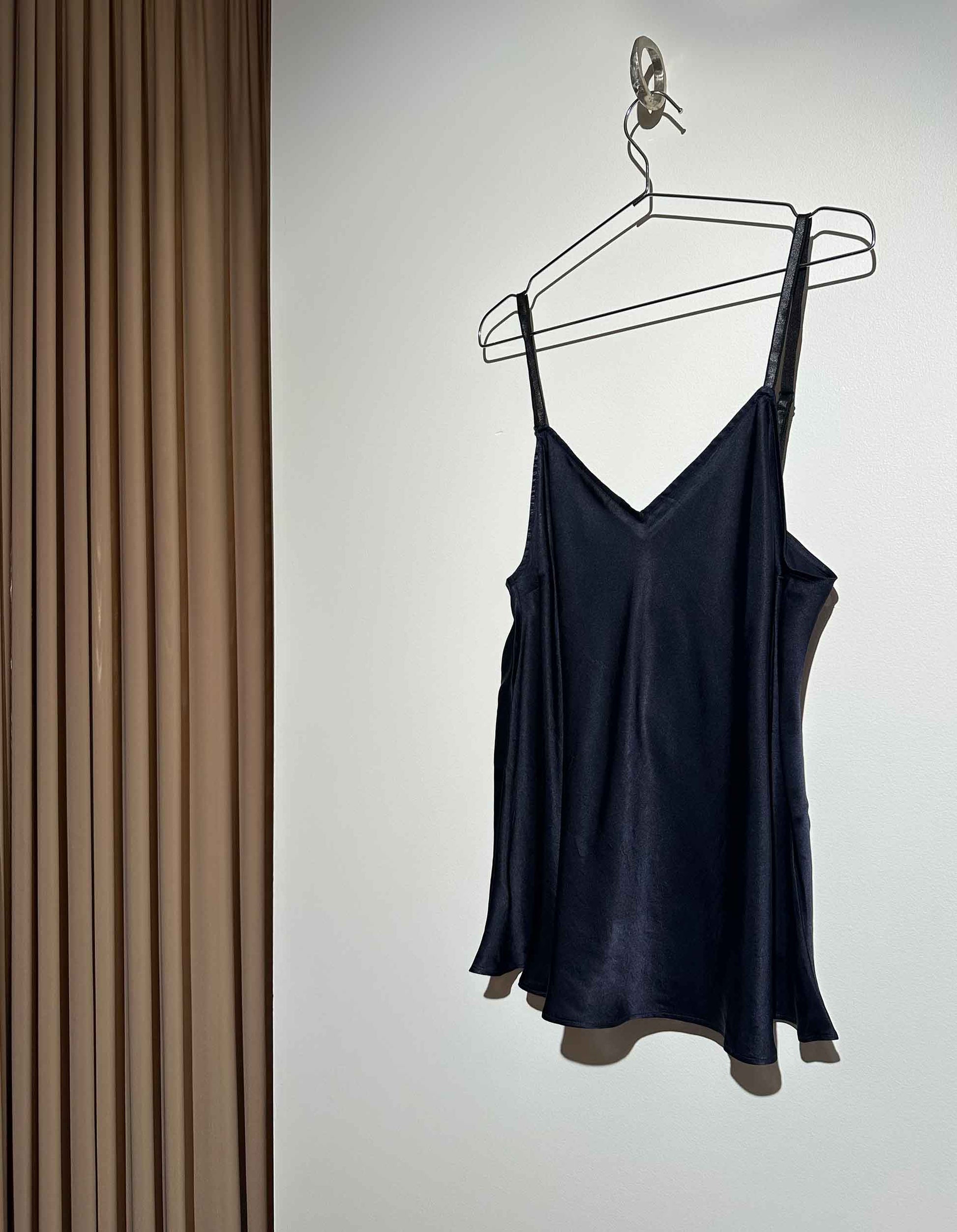 Black slip dress on a hanger against a neutral background