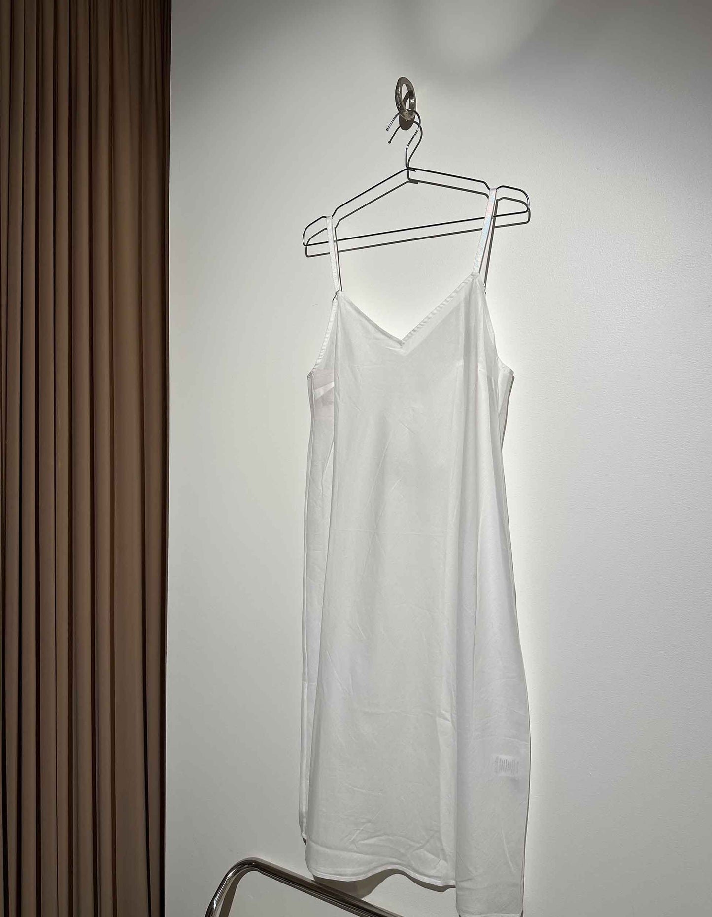 White slip dress hanging on a hanger against a plain wall.