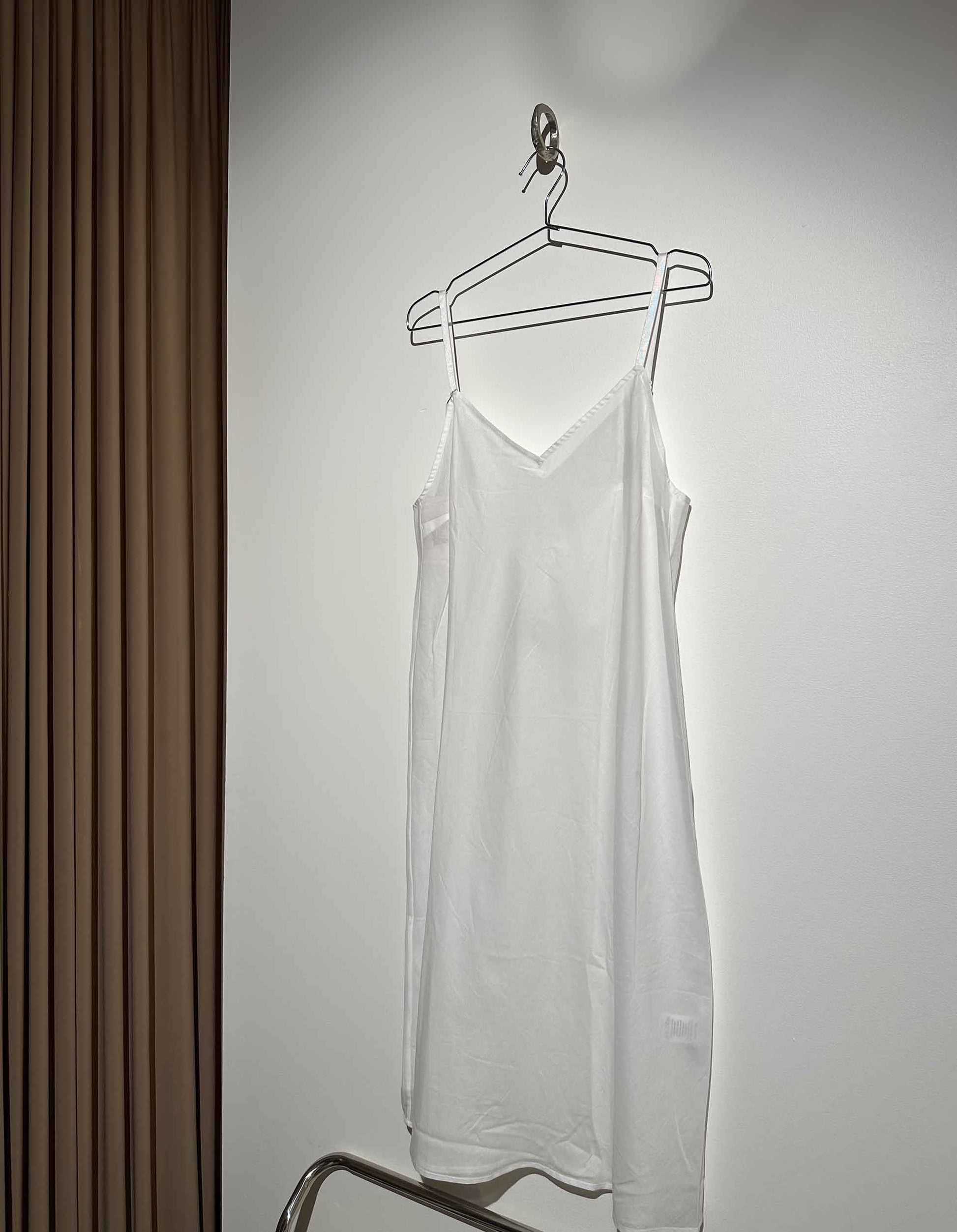 White slip dress hanging on a hanger against a plain wall.