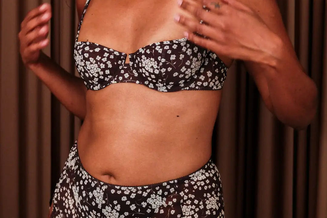 Person wearing a black floral bikini set against a brown curtain background